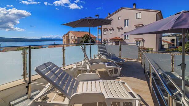 A terrace with sun loungers, umbrellas, and a view of the sea and buildings. - Cozy vacation apartment with pool and terrace in Crikvenica (Crikvenica)