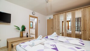 A hotel room with a bed, a wooden bench, a TV, a mirror, and a potted plant. - Cozy vacation apartment with pool and terrace in Crikvenica (Crikvenica)