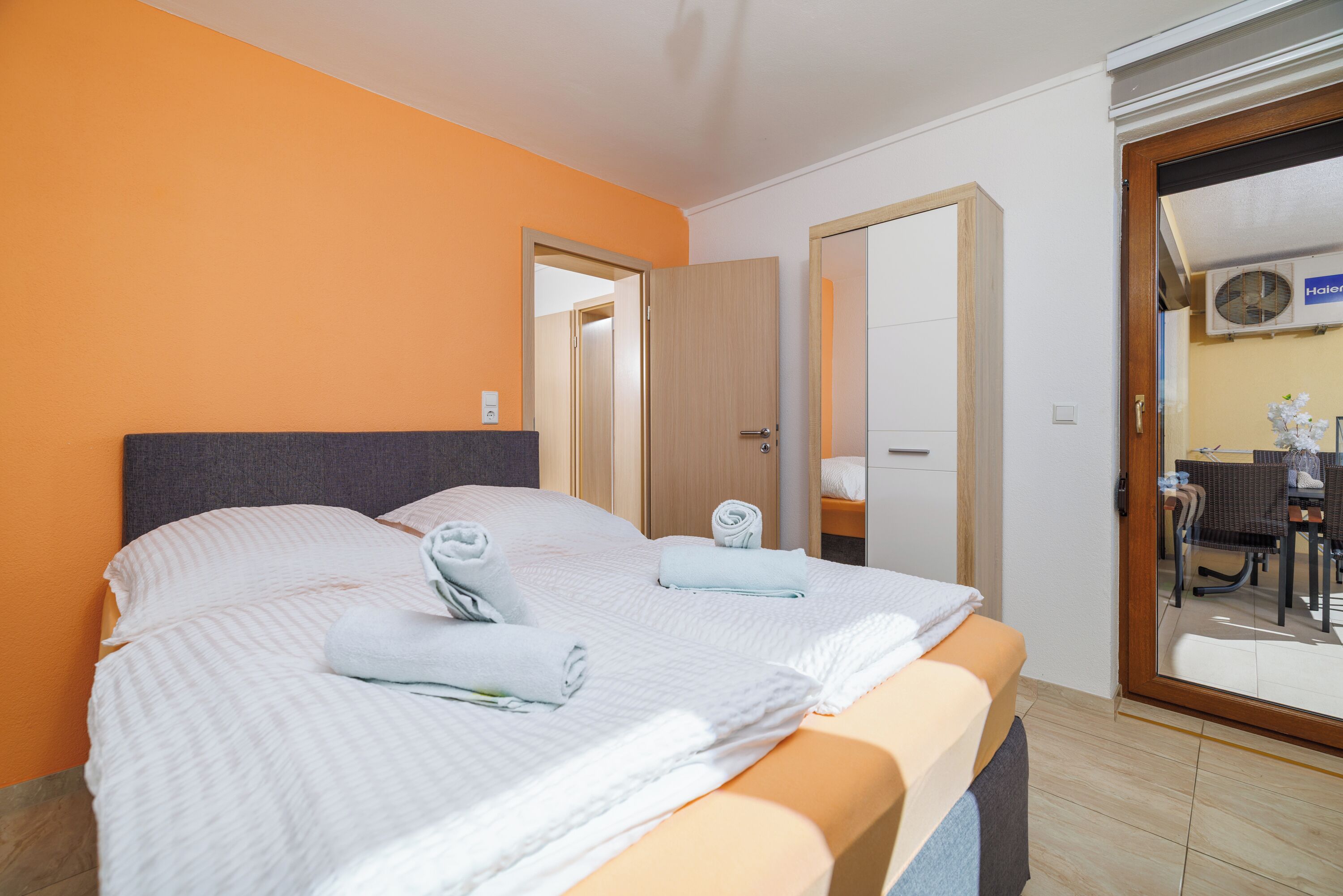 A hotel room with a bed, a door, and a view of an outdoor seating area.