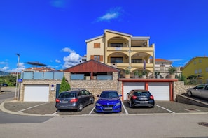 A multi-story building with a stone facade, a red roof, and a parking area with three cars. - Cozy vacation apartment with pool and terrace in Crikvenica (Crikvenica)