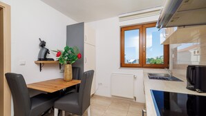 A compact kitchen with a dining table, chairs, a coffee maker, and a view through the window. - Cozy vacation apartment with pool and terrace in Crikvenica (Crikvenica)