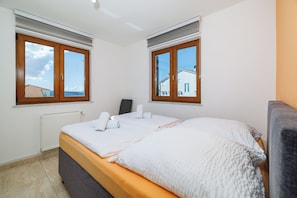 A bedroom with a bed, two windows, a radiator, and a view of the outside. - Cozy vacation apartment with pool and terrace in Crikvenica (Crikvenica)