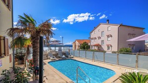 A swimming pool with lounge chairs, a palm tree, and a building with a red-tiled roof. - Cozy vacation apartment with pool and terrace in Crikvenica (Crikvenica)