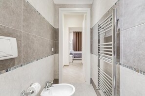 Ein schmales Badezimmer mit Waschbecken, Toilettenpapier und einem Handtuchhalter.
