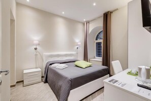 Ein modernes Hotelzimmer mit einem großen Bett, Nachttischlampen, einem Schreibtisch mit Kaffeemaschine und einem mit Vorhängen versehenen Fenster.