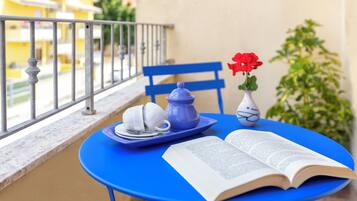 A blue table with a book, teapot, cups, and a vase with flowers on a balcony.