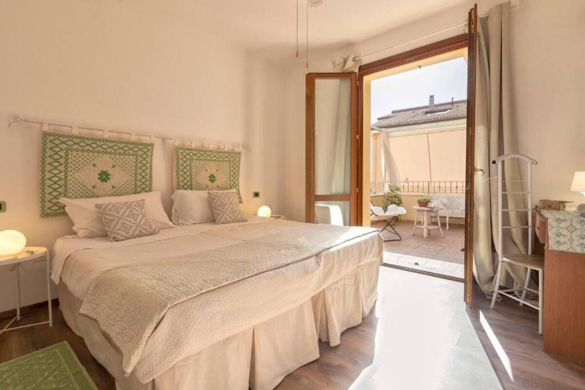 Una camera da letto con un letto, comodini, un balcone con sedie e vista sugli edifici.