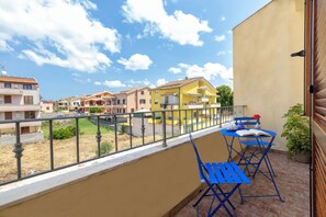 Un balcó amb caires blaus i una taula, amb vista a una zona residencial de cases.