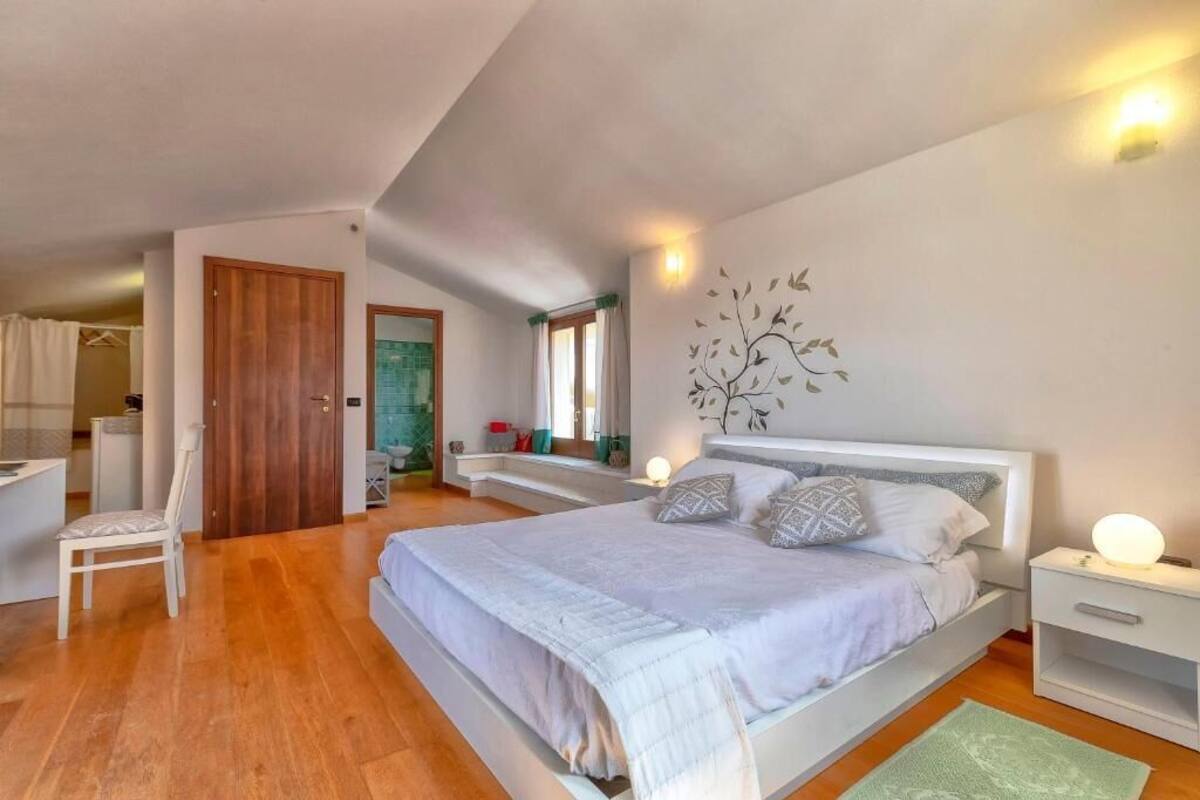 Una camera da letto con un letto, comodini, una sedia, uno specchio e un elemento decorativo a parete.