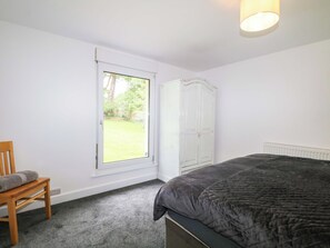 A bedroom with a bed, a chair, a wardrobe, and a window with a view of a garden. - Woodside (Battle)
