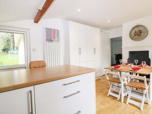 A modern kitchen with white cabinets, a wooden countertop, and a dining area with white chairs and red bowls.