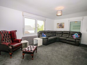 A living room with a red leather armchair, a black leather sofa, and a small ottoman. There is a window with blinds, a ceiling light, and a framed picture on the wall. - Woodside (Battle)