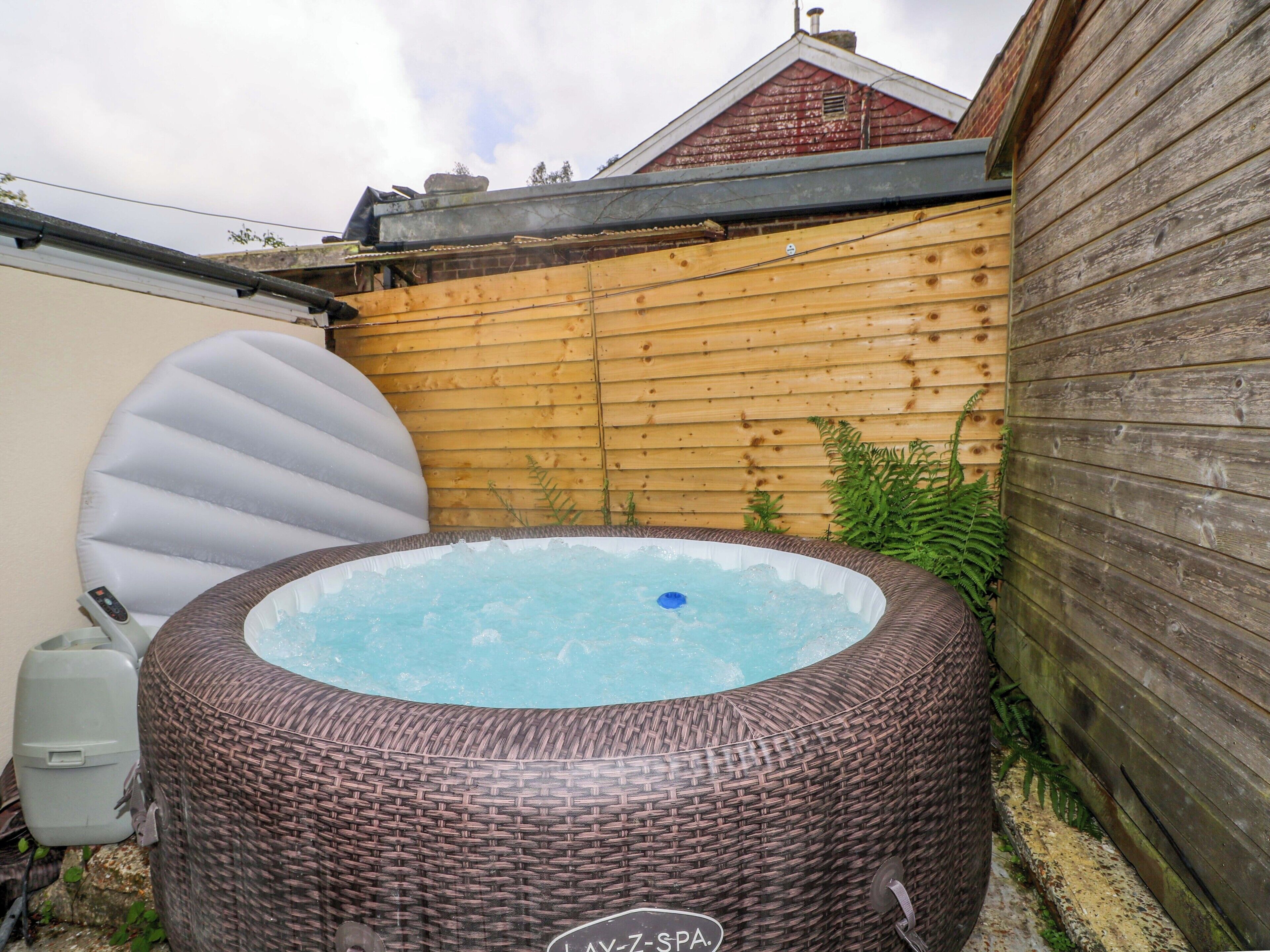 A hot tub in a backyard with a wooden fence and a brick wall.