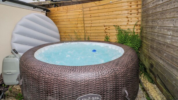 Ett bubbelbad i en trädgård, med ett staket av trä och en mur av tegelsten.