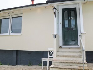 Un edificio con puerta verde, escalones blancos y una silla blanca en el exterior.