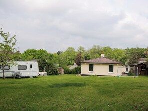 Un patio cubierto de césped con una caravana blanca, una casa pequeña y una portería de fútbol.