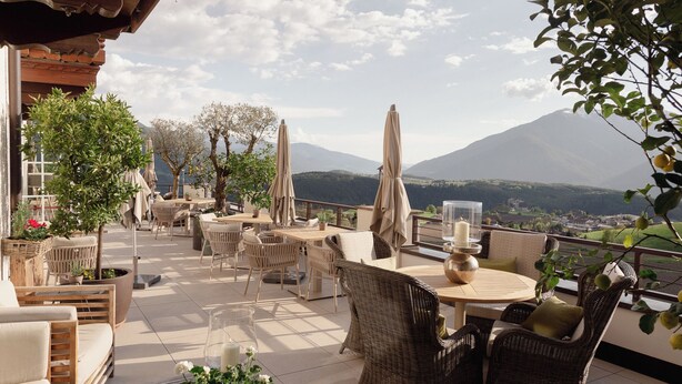 Eine Terrassengruppe im Freien mit Korbmöbeln, Sonnenschirmen und Blumentöpfen.