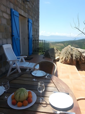 A dining table with chairs, a plate of fruit, and wine glasses, overlooking a scenic landscape.
