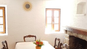Un comedor con una mesa, sillas, un florero con flores, una chimenea y un adorno con motivo de sol en la pared.