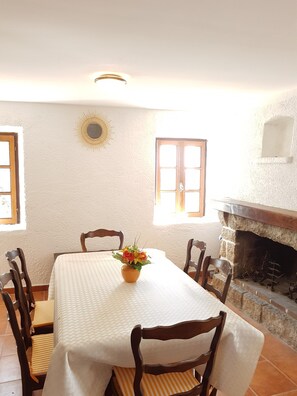 A dining area with a table, chairs, a vase with flowers, a fireplace, and a sunburst decoration on the wall.