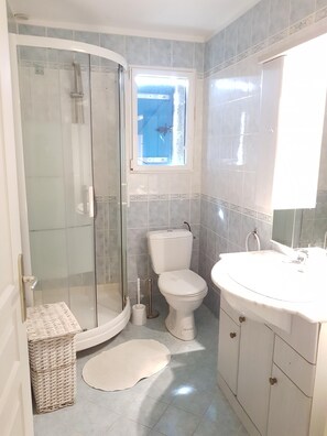 Ein Badezimmer mit einer Duschkabine, einer Toilette, einem Waschbecken und einem Fenster.