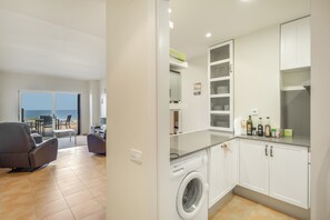 A modern kitchen with a washing machine, a dining area with a view, and a balcony with outdoor furniture. - Apartment 'Sa Calma I Bajos D' with Sea View, Wi-Fi and Air Conditioning (Begur)