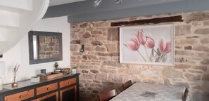 Ein Essbereich mit einer Steinwand, einem gerahmten Blumenbild, einem Holztisch und einem Spiegel an der Wand.