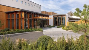 A modern building with a covered walkway, large windows, and a landscaped area with shrubs and trees. - The Grace Wesport Estate  (Westport)