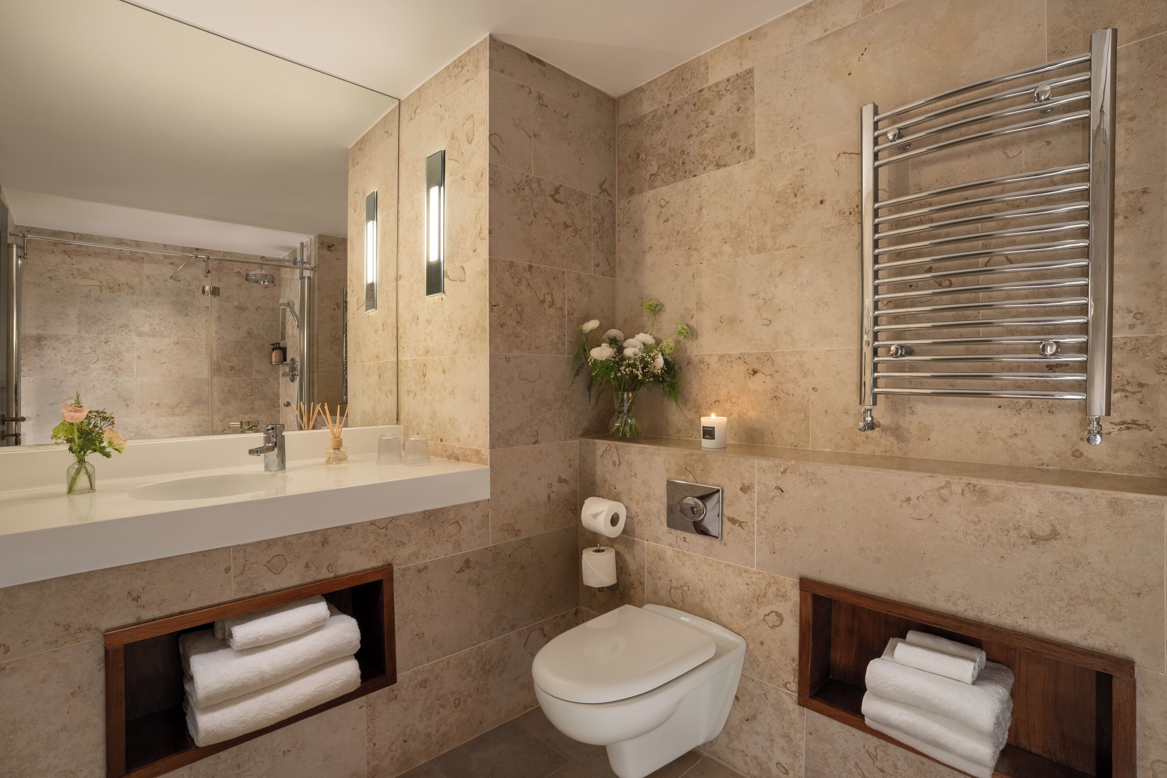 A modern bathroom with a large mirror, a shower, a toilet, and towel racks.