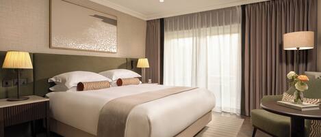 A hotel room with a large bed, bedside lamps, a chair, a table with a vase of flowers, and a painting on the wall.