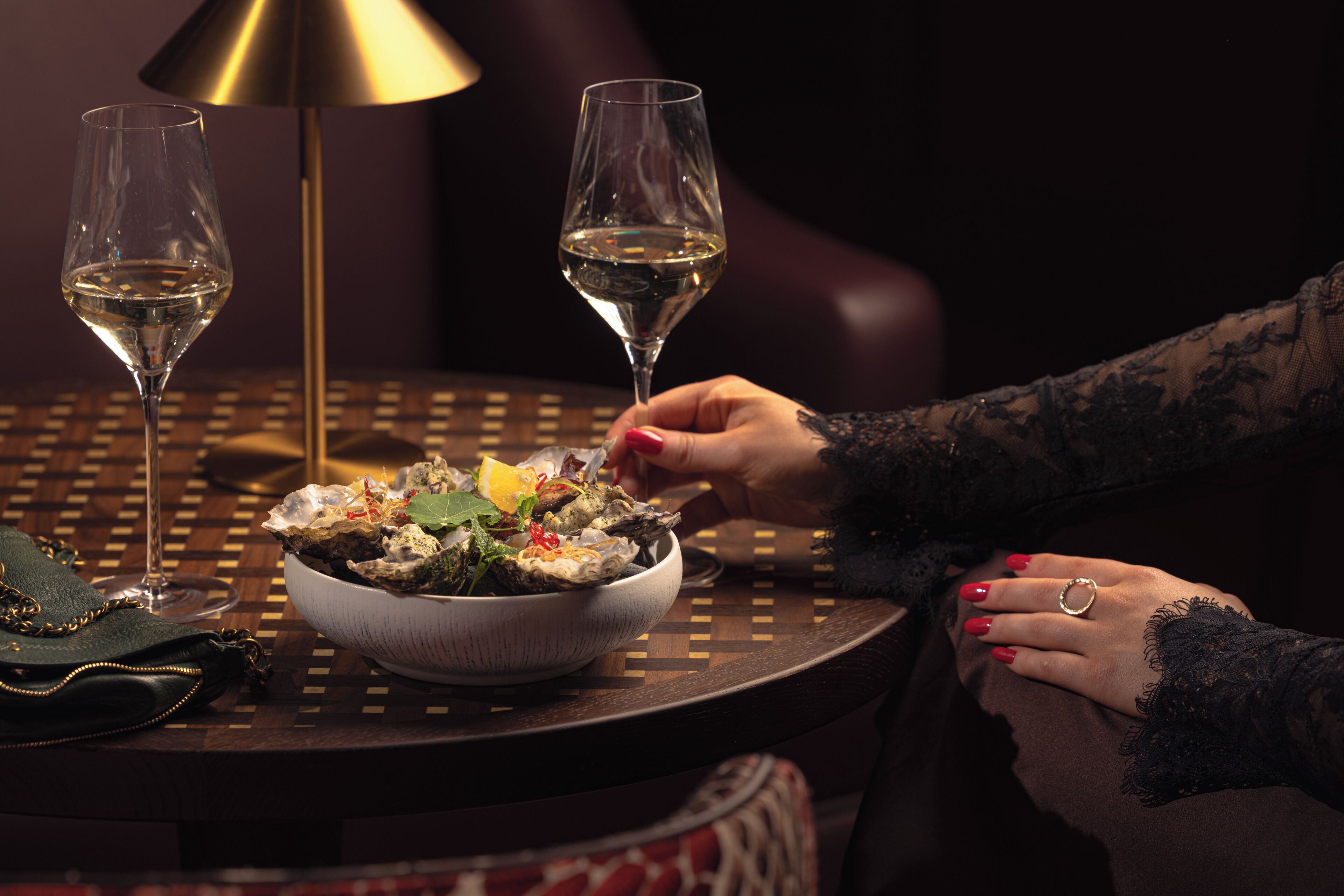 A dining table with a bowl of oysters, two wine glasses, and a lamp.