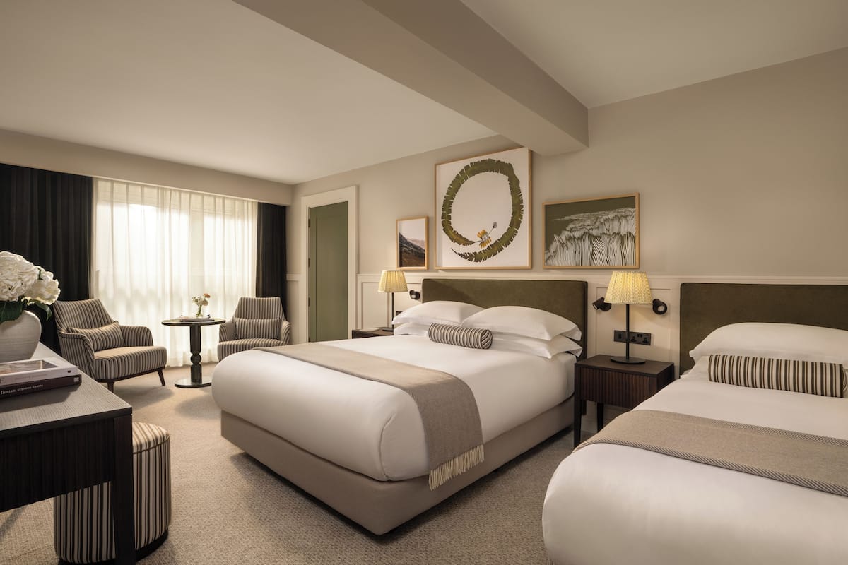 A hotel room with a large bed, two armchairs, a small table, and a nightstand with lamps.