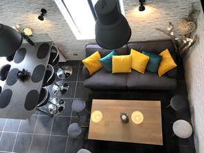 A modern interior with a grey sofa, yellow and teal cushions, a wooden coffee table, and a dining area with a round table and chairs. - Holiday Home “Gîte L'atelier Au Cœur De La Baie” with Wi-Fi (Boismont)
