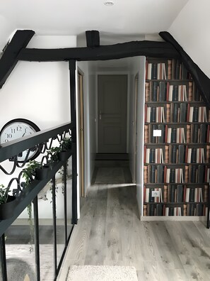 A staircase with a wooden floor, a black metal railing, and a bookshelf filled with books. - Holiday Home “Gîte L'atelier Au Cœur De La Baie” with Wi-Fi (Boismont)