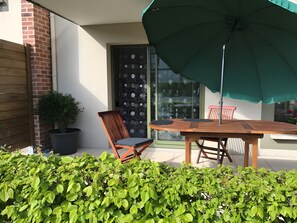 Eine Terrasse mit Holztisch und -stühlen, einem grünen Sonnenschirm und einem Blumentopf.