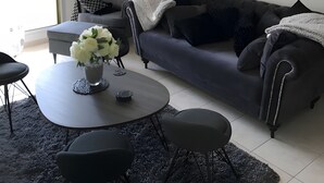 Moderni olohuone, jossa on harmaa sohva, pyöreä sohvapöytä ja kattokruunu.