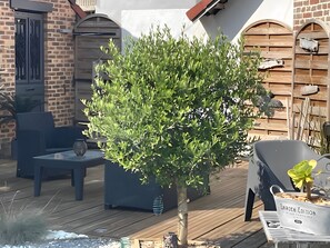 En patio med et lille træ, en blå stol og en hvid trillebør med teksten 'GABOEN EDITION'.