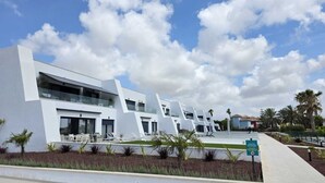 Ein modernes Gebäude mit weißer Fassade, mehreren Balkonen und einem Poolbereich mit Liegestühlen.