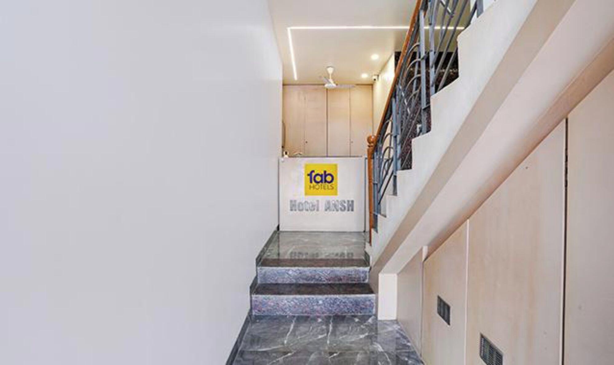 A hotel interior with a marble staircase, a sign for 'fab hotels,' and a ceiling fan.