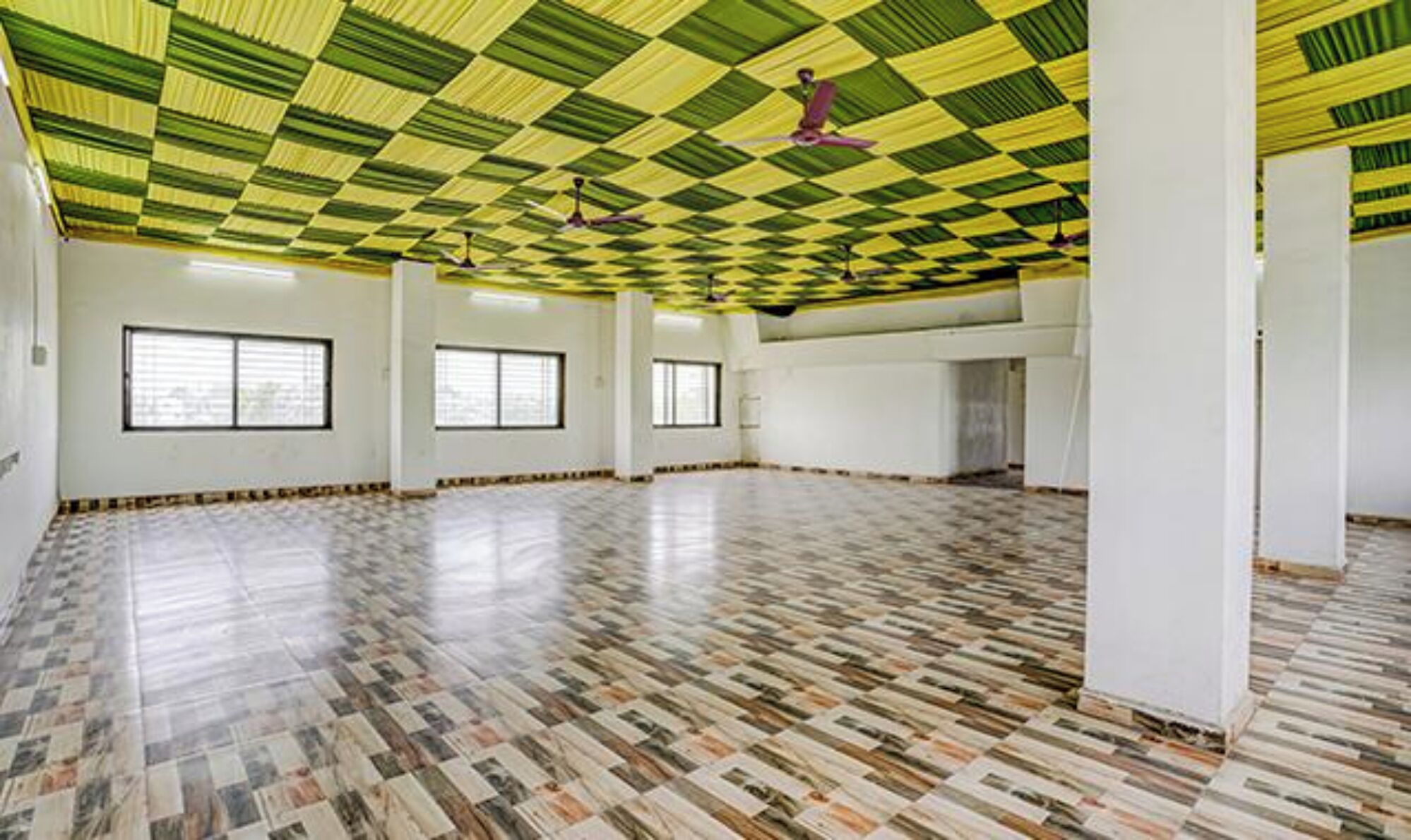 A large, empty room with a patterned floor, white walls, and a green and yellow checkered ceiling.