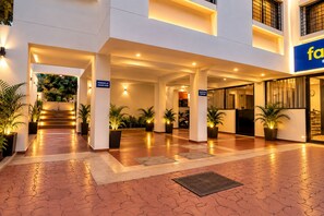 A hotel entrance with a covered walkway, potted plants, and a sign indicating parking at owner risk. - FabHotel Galaxy Apartment (Pune)