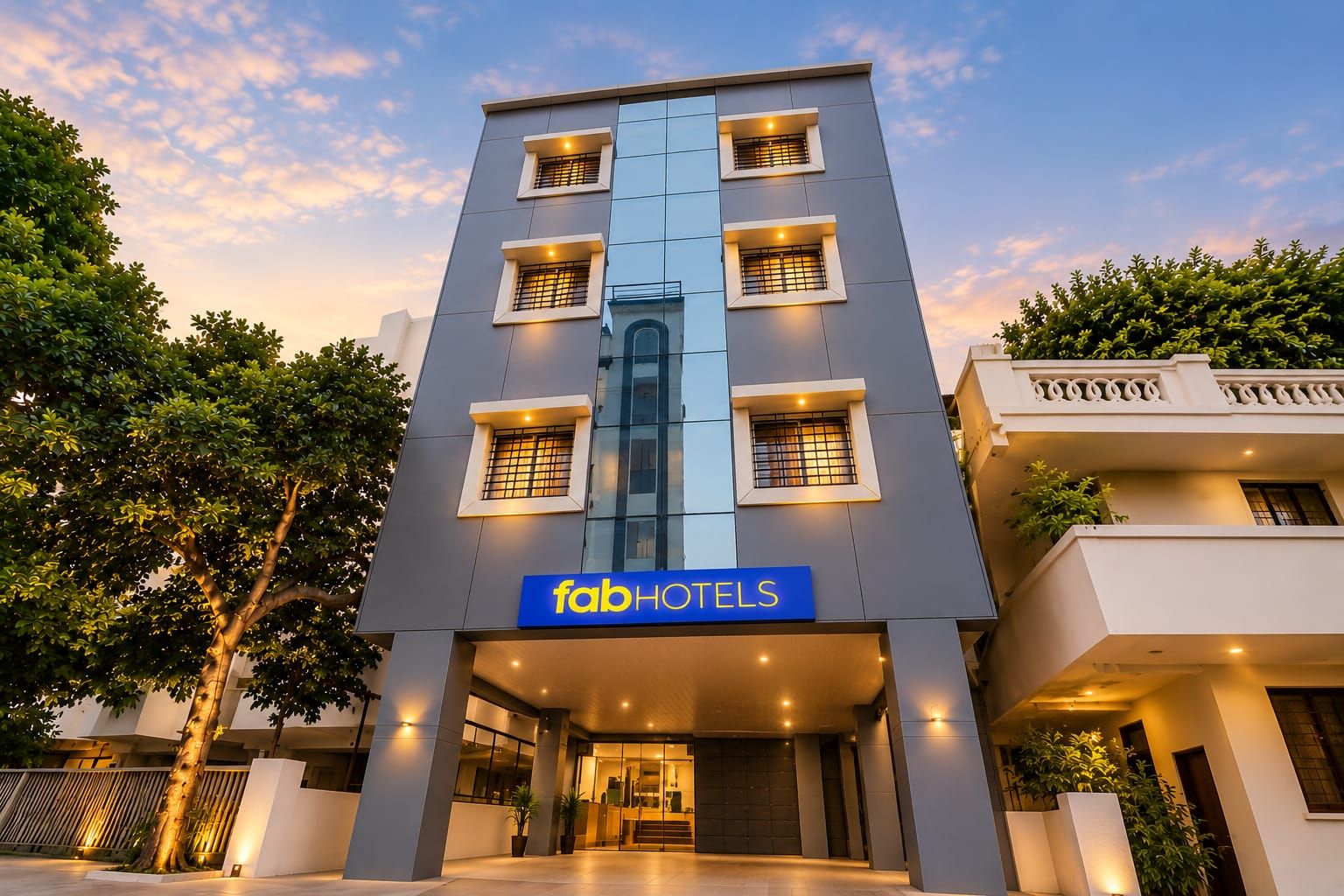 A modern hotel building with a prominent 'fabHOTELS' sign, multiple windows, and a well-lit entrance.