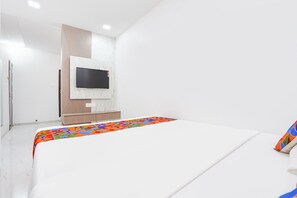 A bedroom with a bed, a TV mounted on a wall, and a door. - FabHotel Galaxy Apartment (Pune)