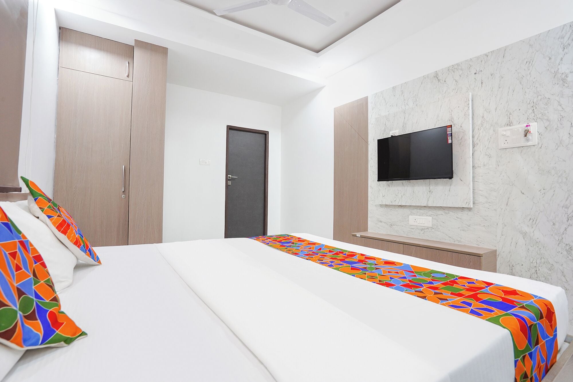 A hotel room with a bed, a TV mounted on the wall, and a door.