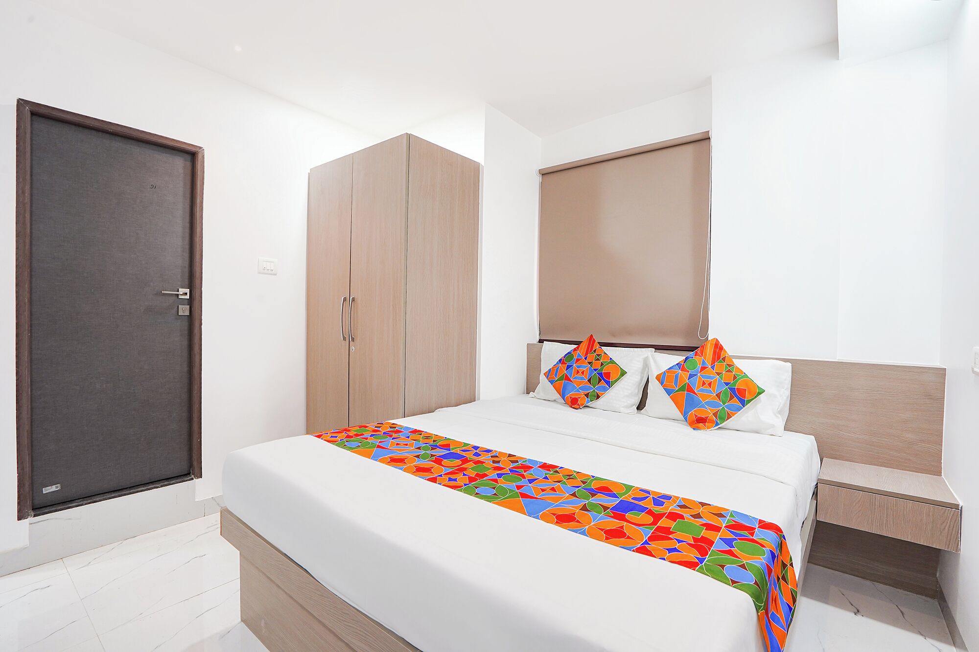 A hotel room with a bed, a wardrobe, and a window with a blind.