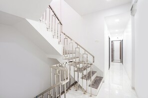 A modern staircase with a glass railing, leading to a landing with a door. - FabHotel Galaxy Apartment (Pune)