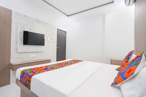 A hotel room with a bed, a TV mounted on the wall, and a door. - FabHotel Galaxy Apartment (Pune)