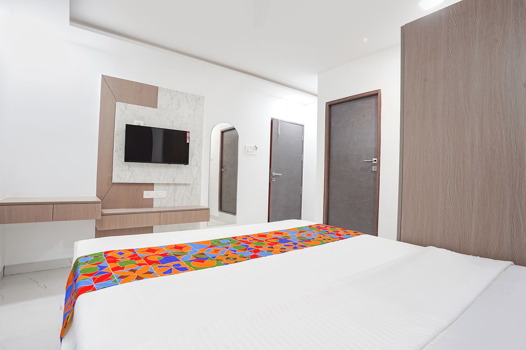 A hotel room with a bed, a television mounted on the wall, a wardrobe, and a door.