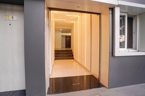 An interior hallway with a staircase leading to a door, a window on the right, and a door number sign. - Via Galaxy Hospitality (Pune)