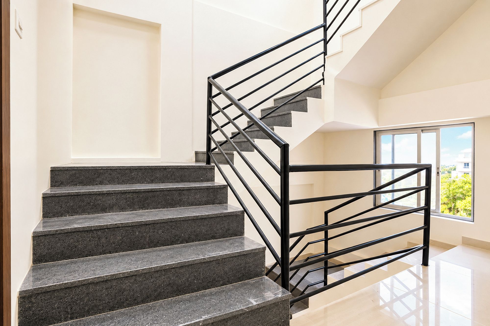 A modern staircase with a black metal railing, leading to a higher floor.